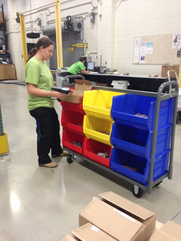 A person picking something from extra large plastic bins stacked on top of each other in a warehouse setting.