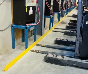 The forks of a fork lift are stopped by a yellow floor-mounted guard rail