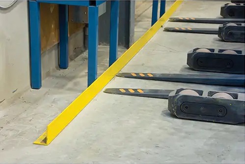 The forks of a fork lift are stopped by a yellow floor-mounted guard rail